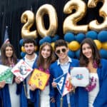 SDJA students in graduation gowns pose with their decorated caps in front of balloons.
