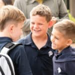 Three boys in SDJA blue polo shirts smile on the first day of school