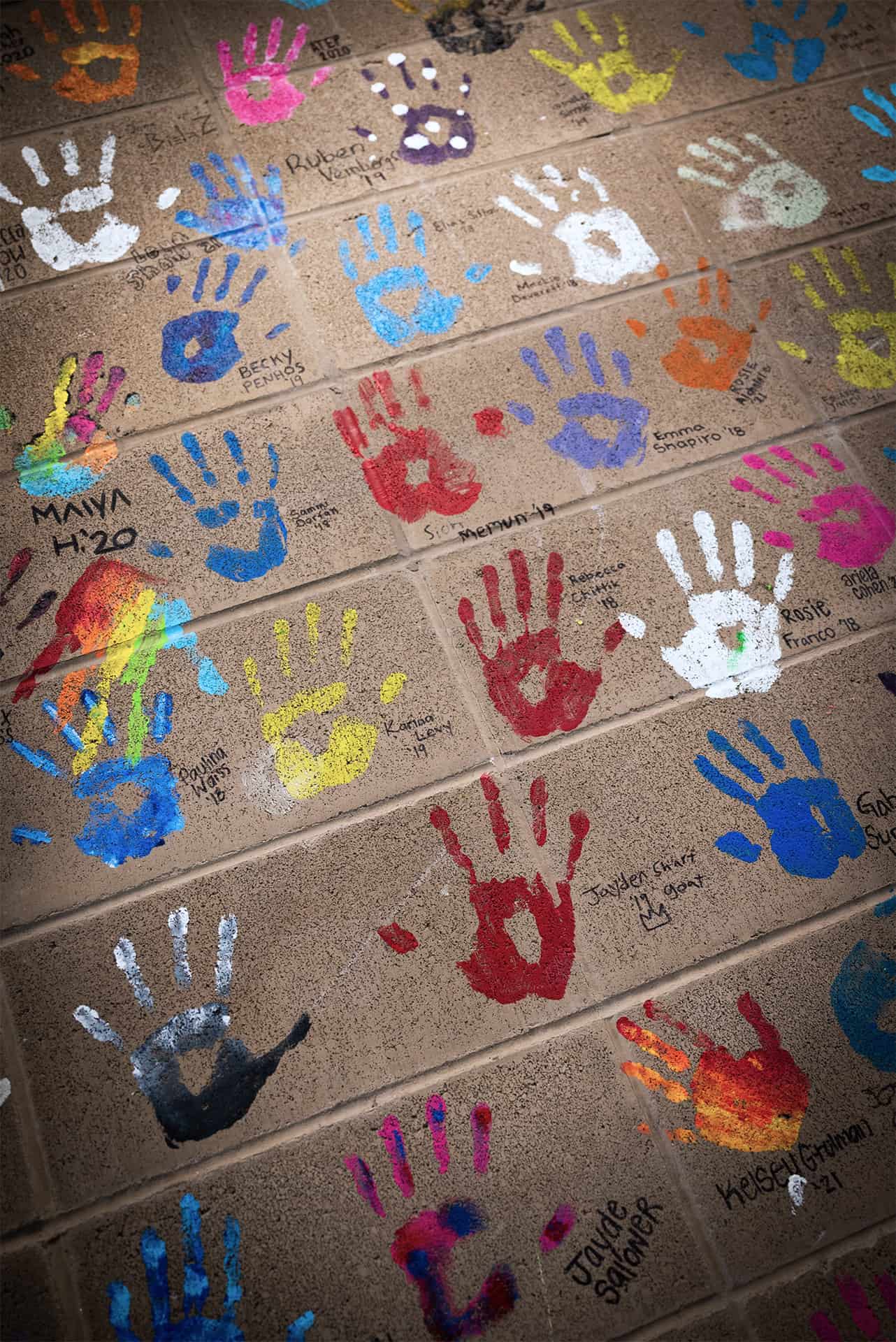 Handprints in different colored paint decorating a brick wall