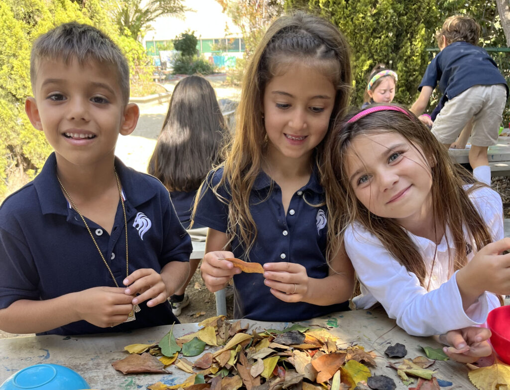 Three lower school students work on a leaf project in the garden