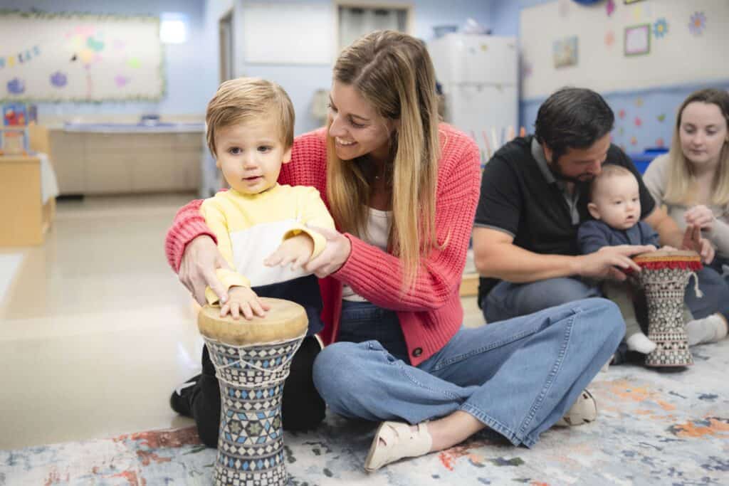 A mother and young child play with a drum during a music class.