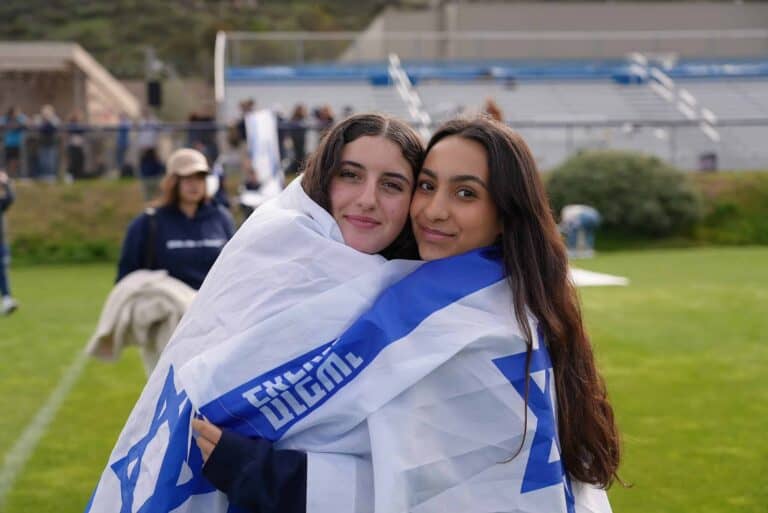 Two students embrace with an Israeli flag wrapped around their shoulders.