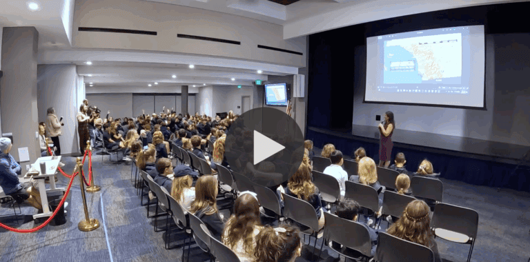 video still of SDJA class listening to a presentation in an auditorium