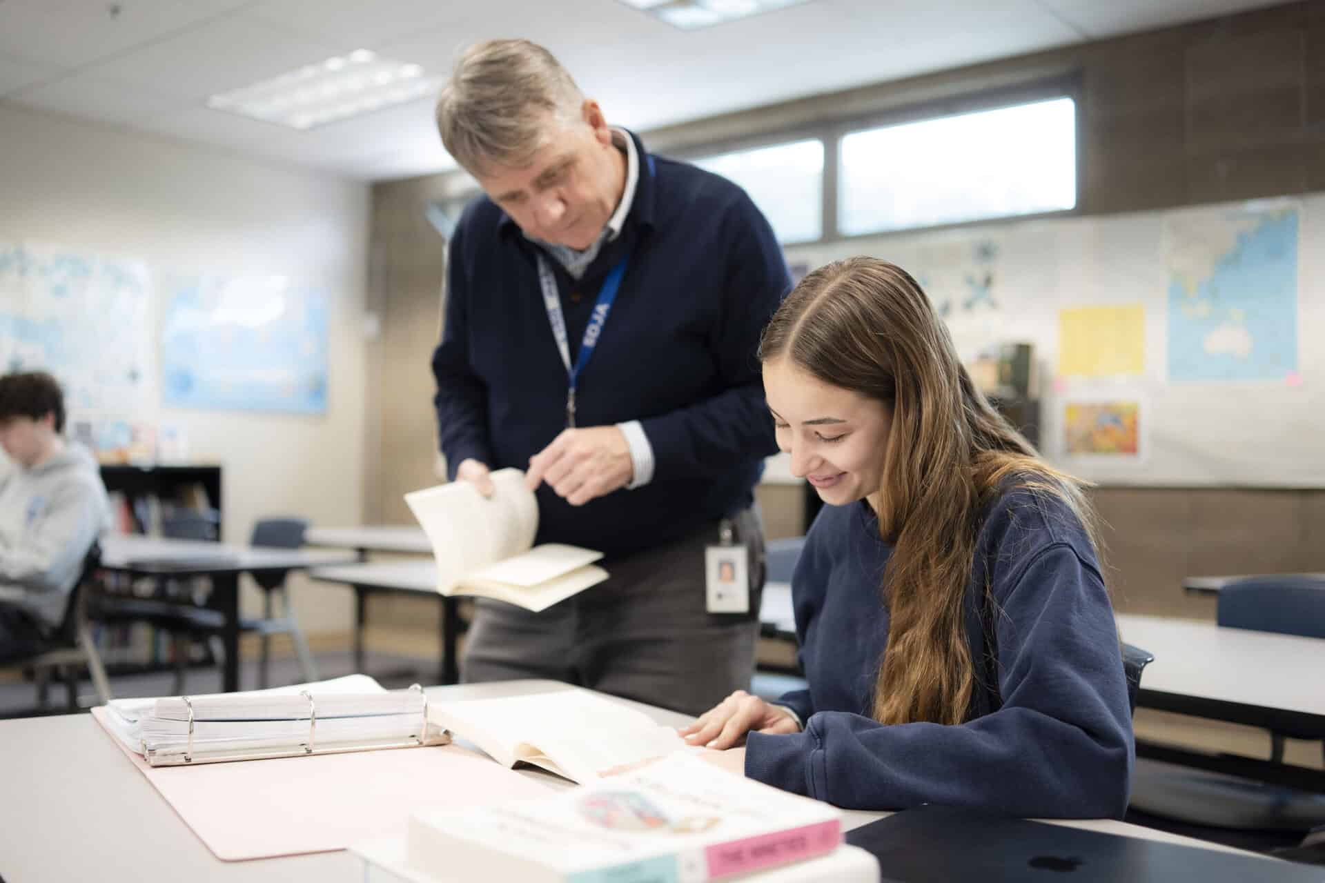 A student working in a classroom receives help from a teacher