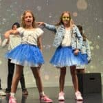 A group of girls in matching outfits singing and dancing on stage.
