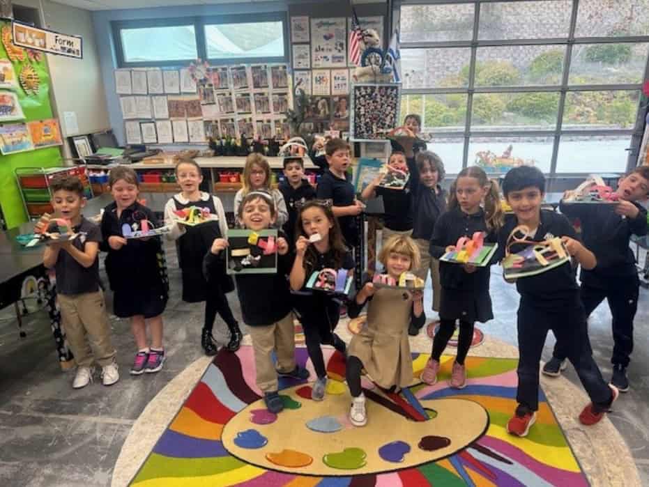A group of students holding up art projects in a classroom