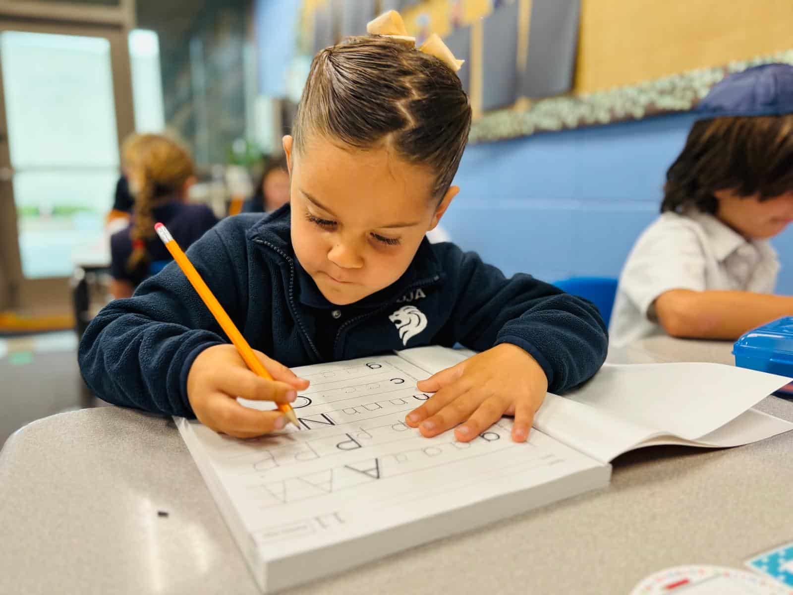 A student practicing writing letters in a workbook.
