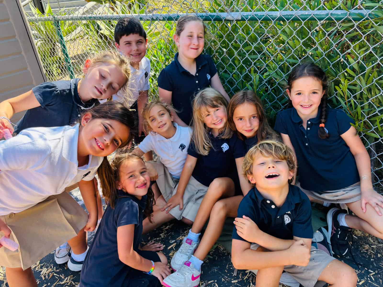 Group of elementary school students posing outdoors against a fence