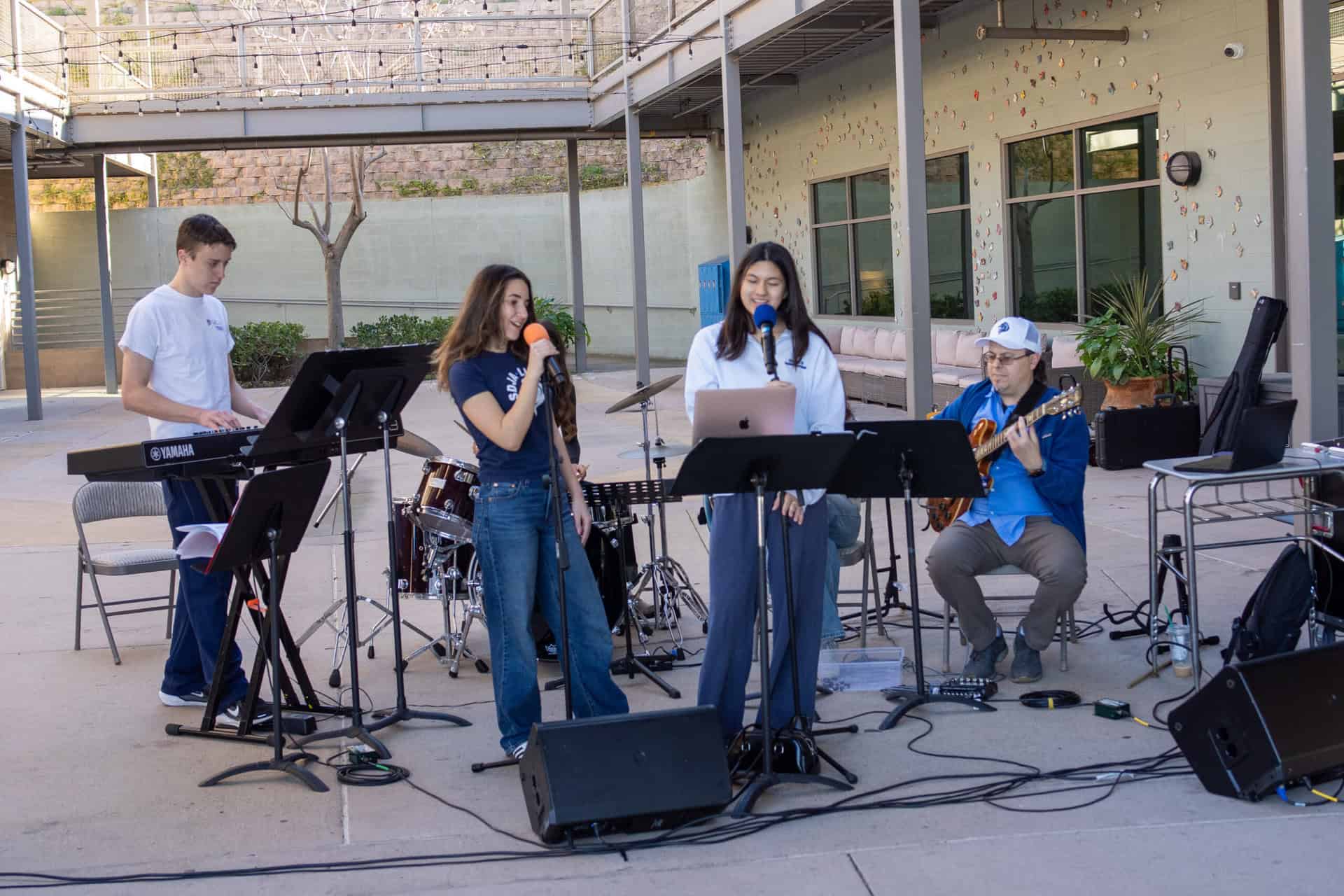 Upper school students performing music outdoors, featuring vocals, guitar, and keyboard