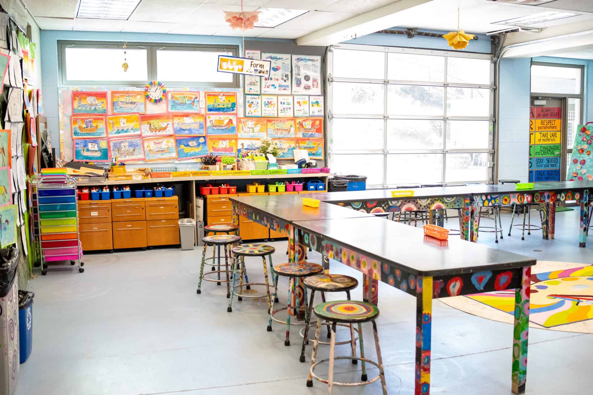 Lower School art classroom, featuring bright colors, hanging artwork, and painted tables and chairs.