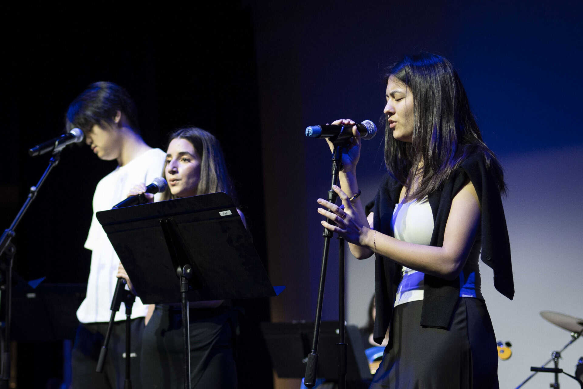 SDJA student singing into a microphone, backed by a band on stage