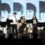 SDJA upper school students performing music on stage, with a slide of the Beatles behind them.