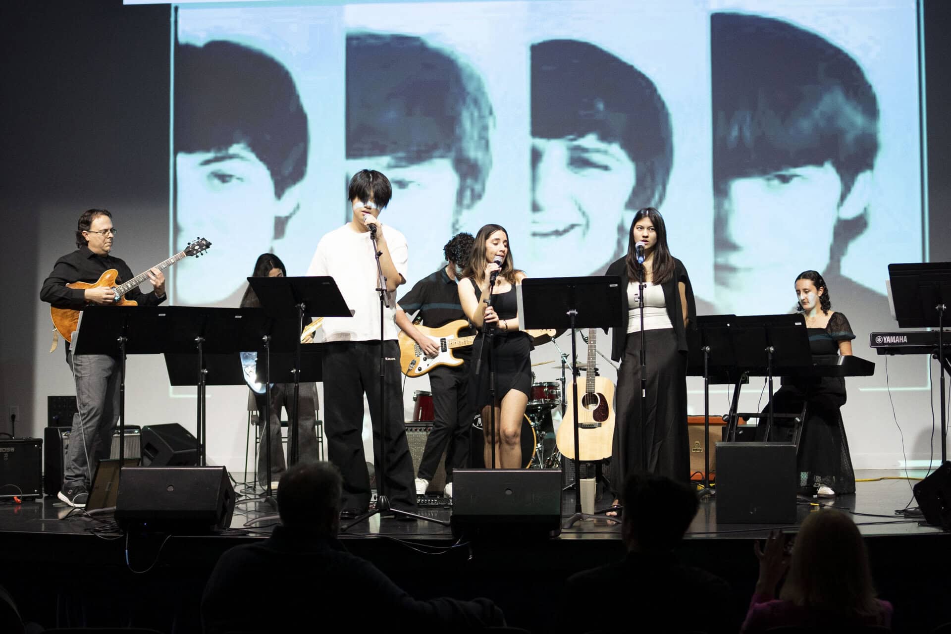 SDJA upper school students performing music on stage, with a slide of the Beatles behind them.