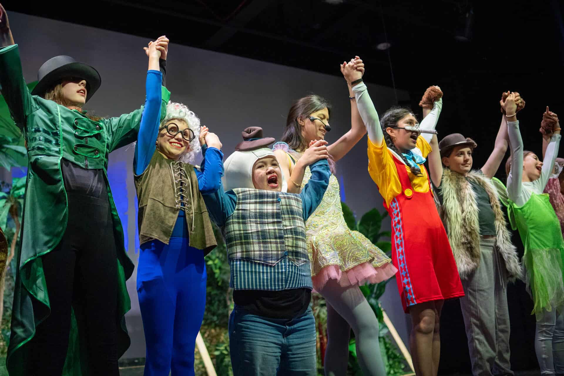 Students in costume, holding up their hands, during a performance of Shrek The Musical