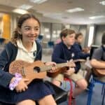 Lower school student smiles while holding a ukulele