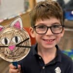 Lower school student smiling and holding up a cute art piece of a cat