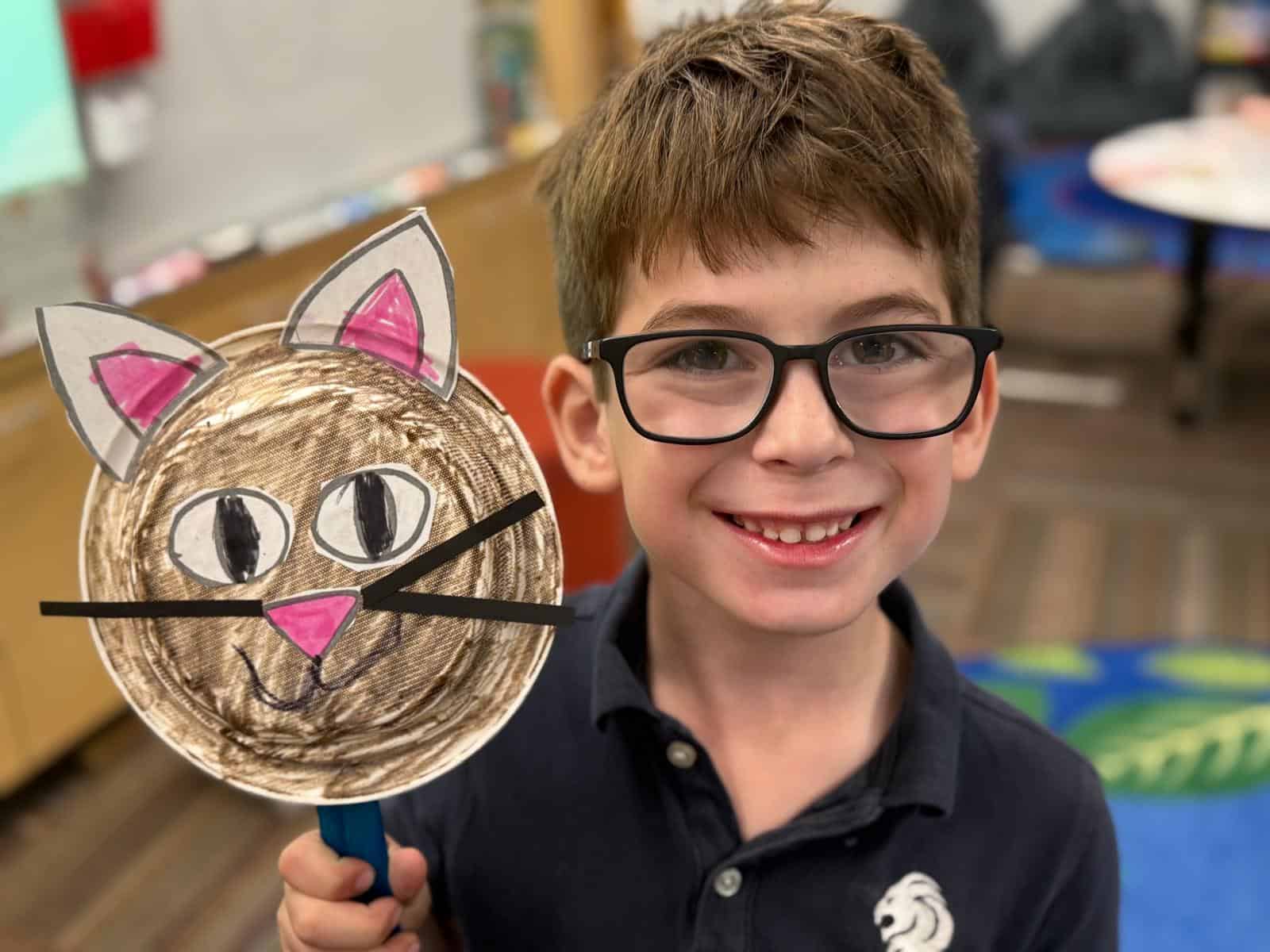 Lower school student smiling and holding up a cute art piece of a cat