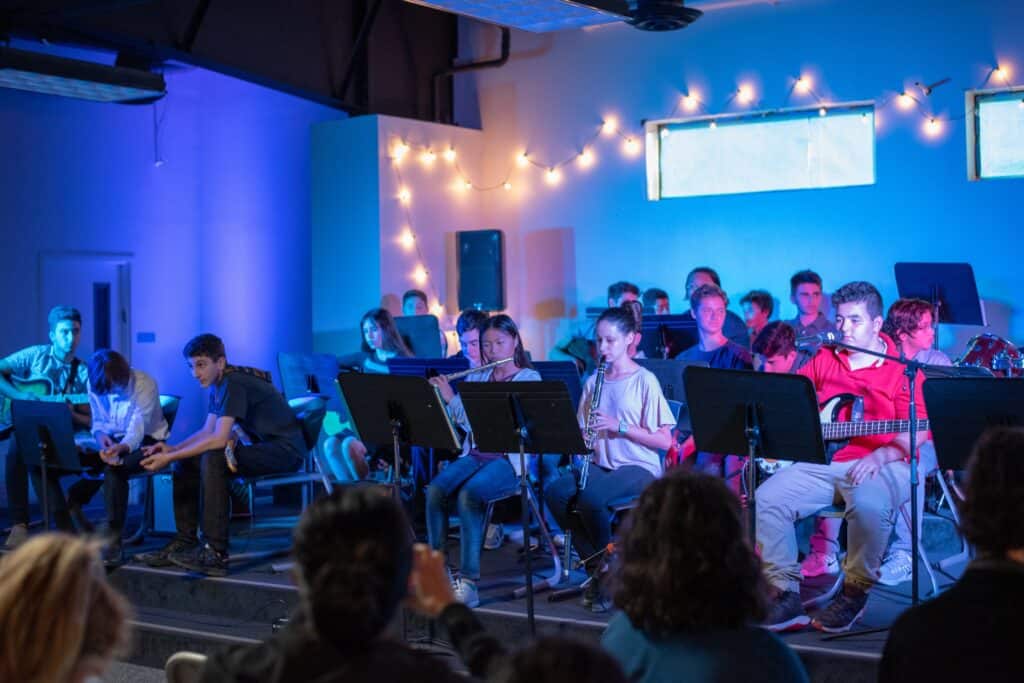 Band students performing on stage with string lights lit up in the background.