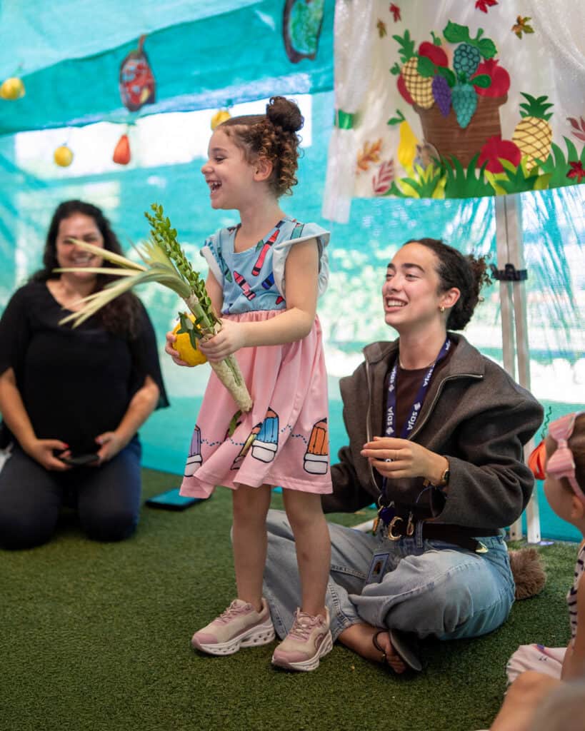 A girl holding a lulav and etrog in a sukkah