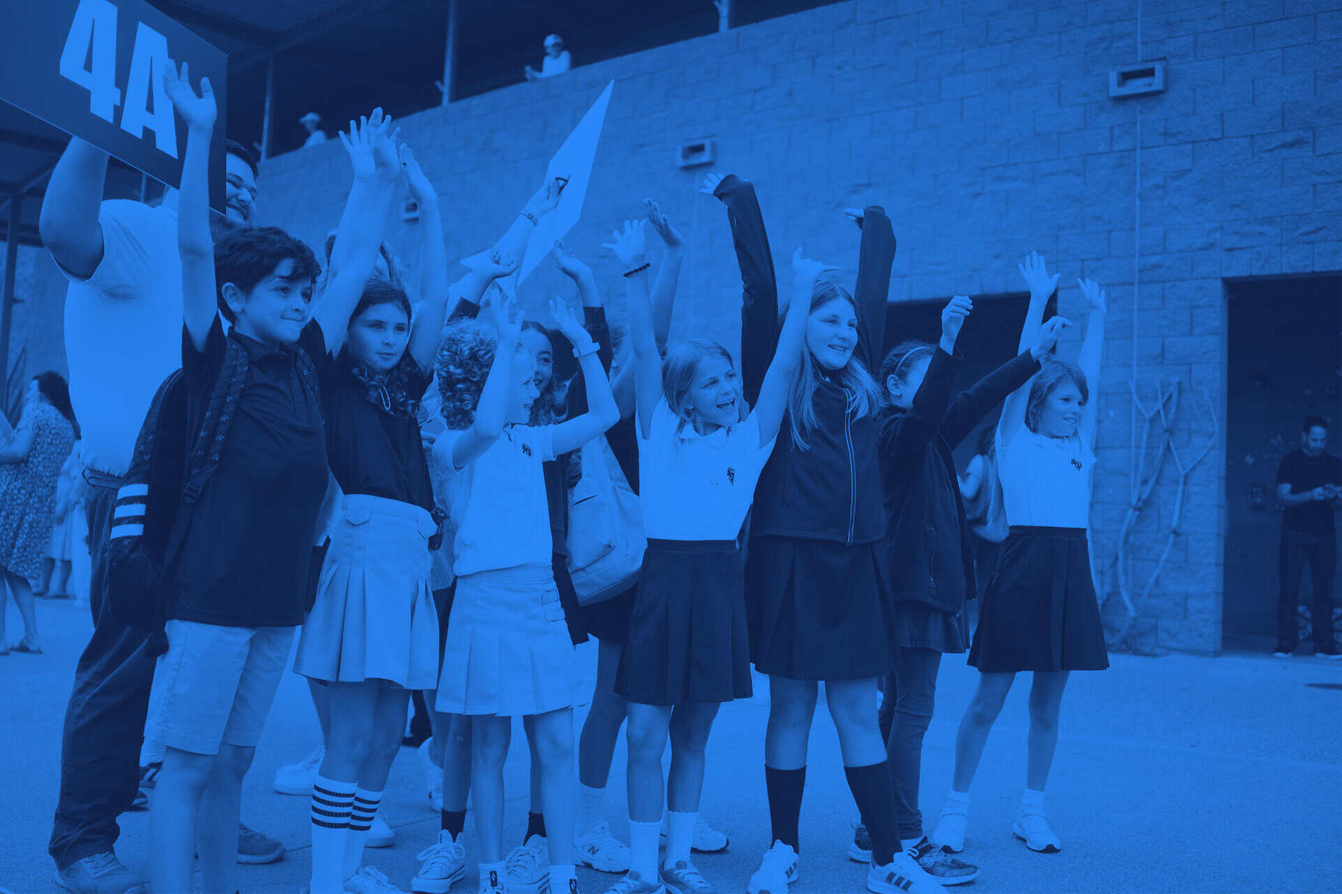 Students standing in a group on the SDJA campus, with their arms in the air.