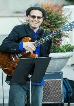 Tommy Collins, smiling and holding a guitar