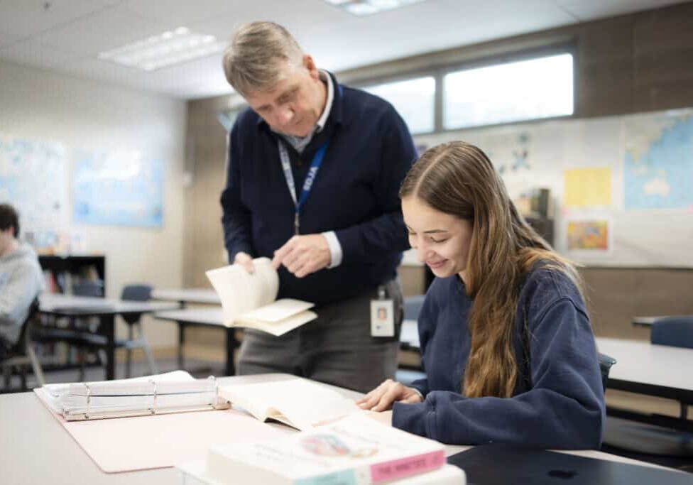 A student working in a classroom receives help from a teacher
