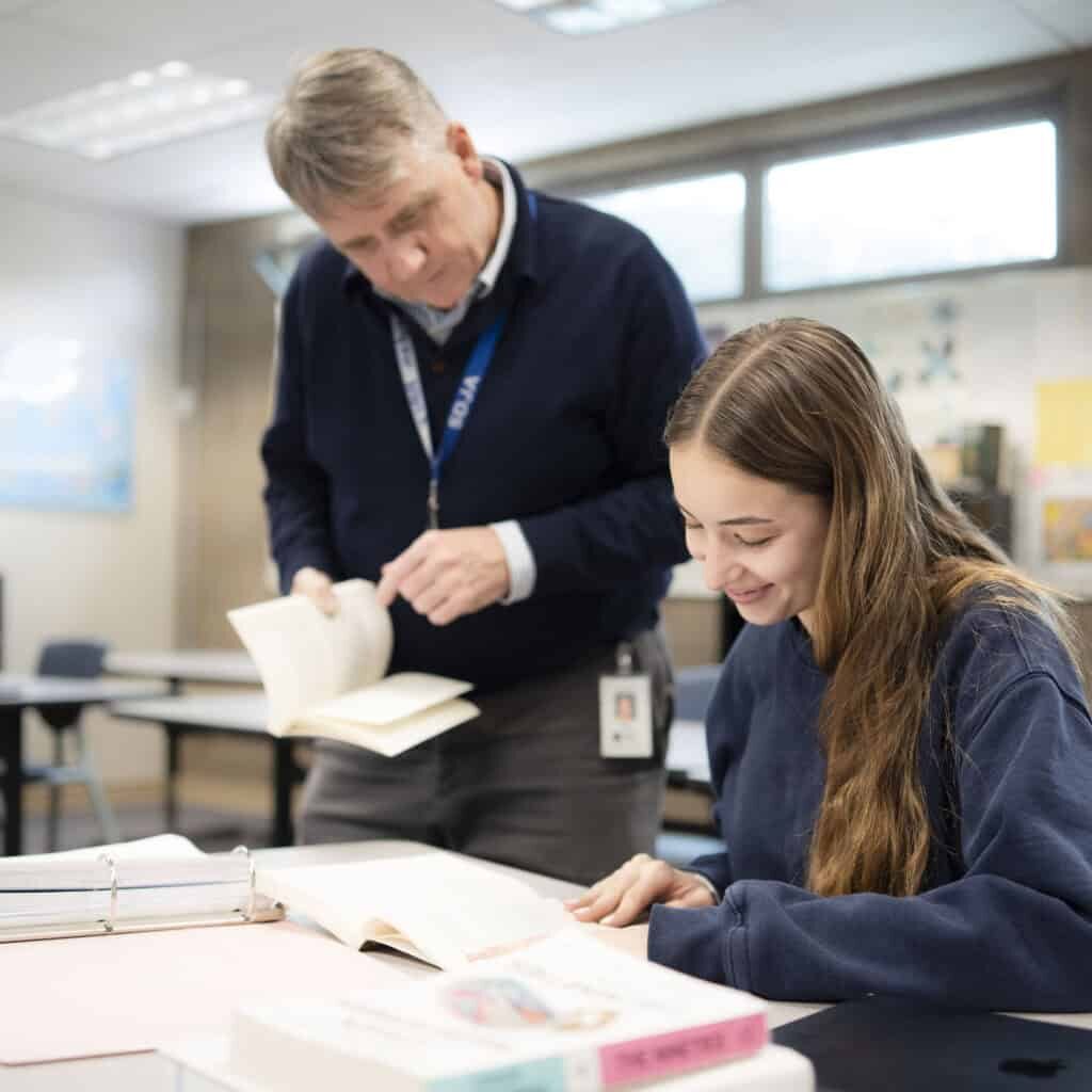 A student working in a classroom receives help from a teacher