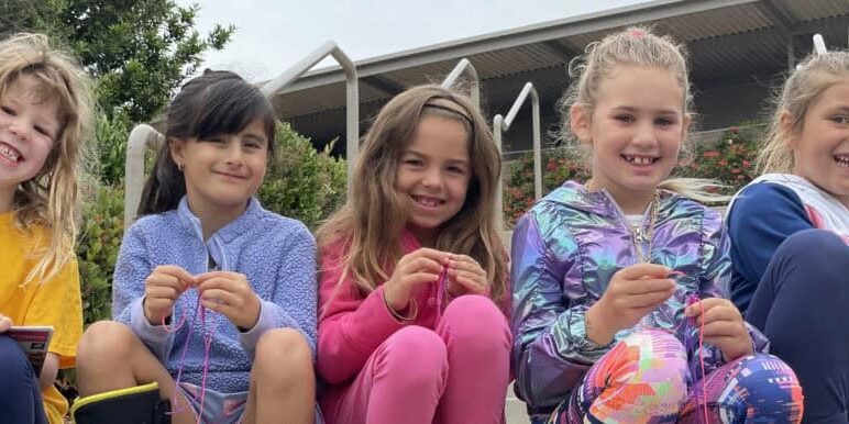 Elementary aged children smiling while seated at an outdoor playground