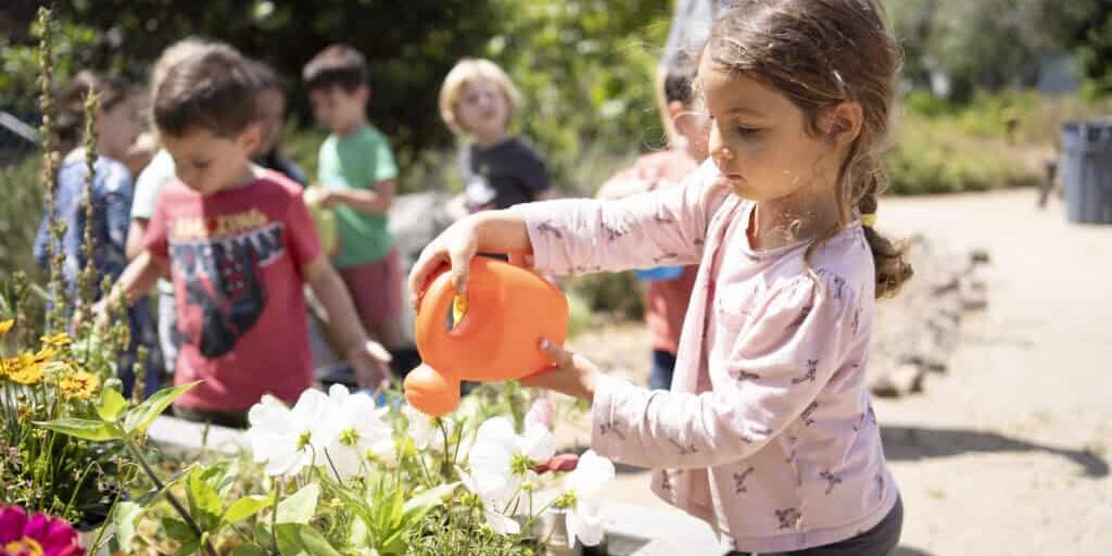 A girl using a watering pail to water flowers
