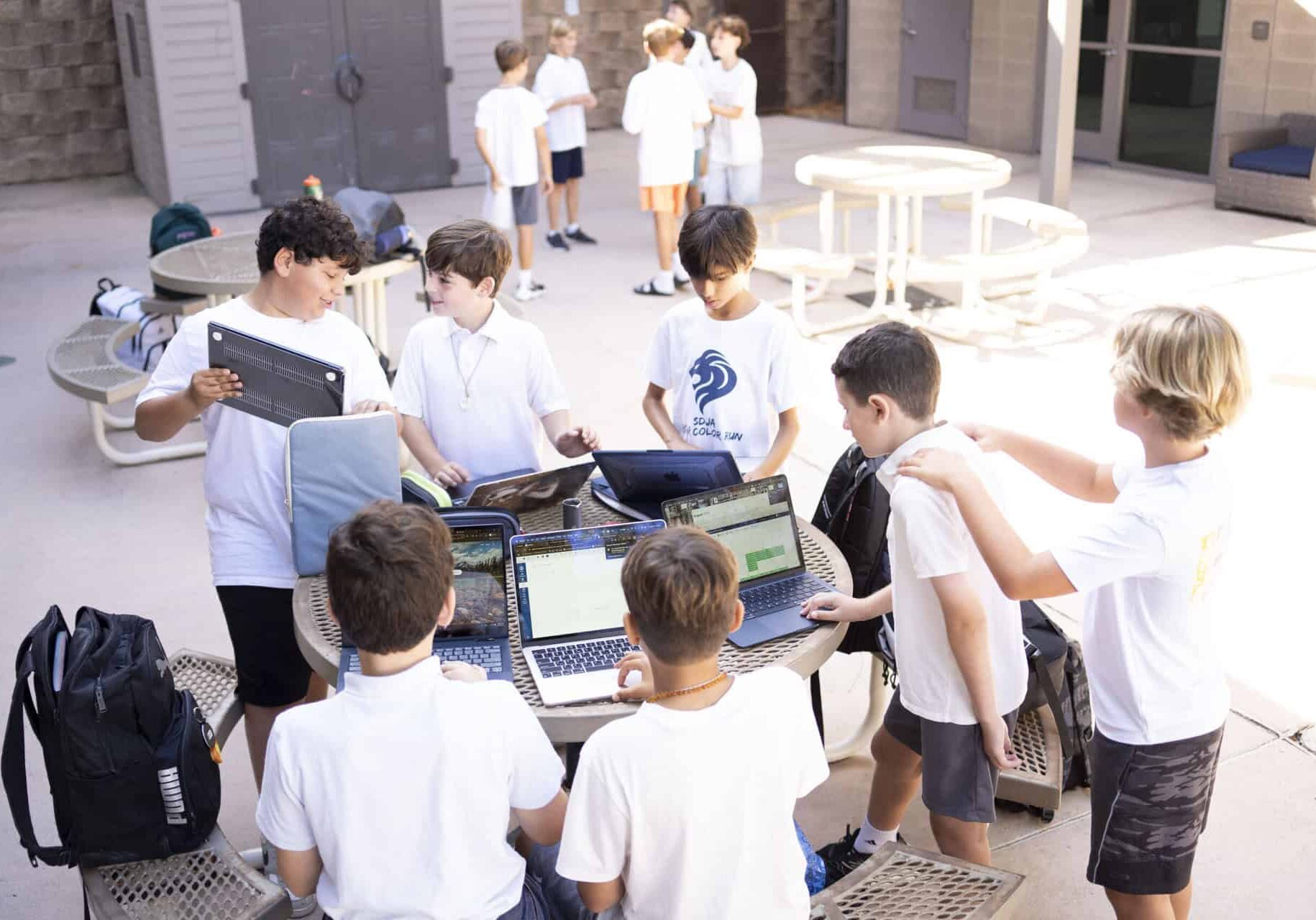 SDJA middle school students gathered at an outdoor table with their laptops.