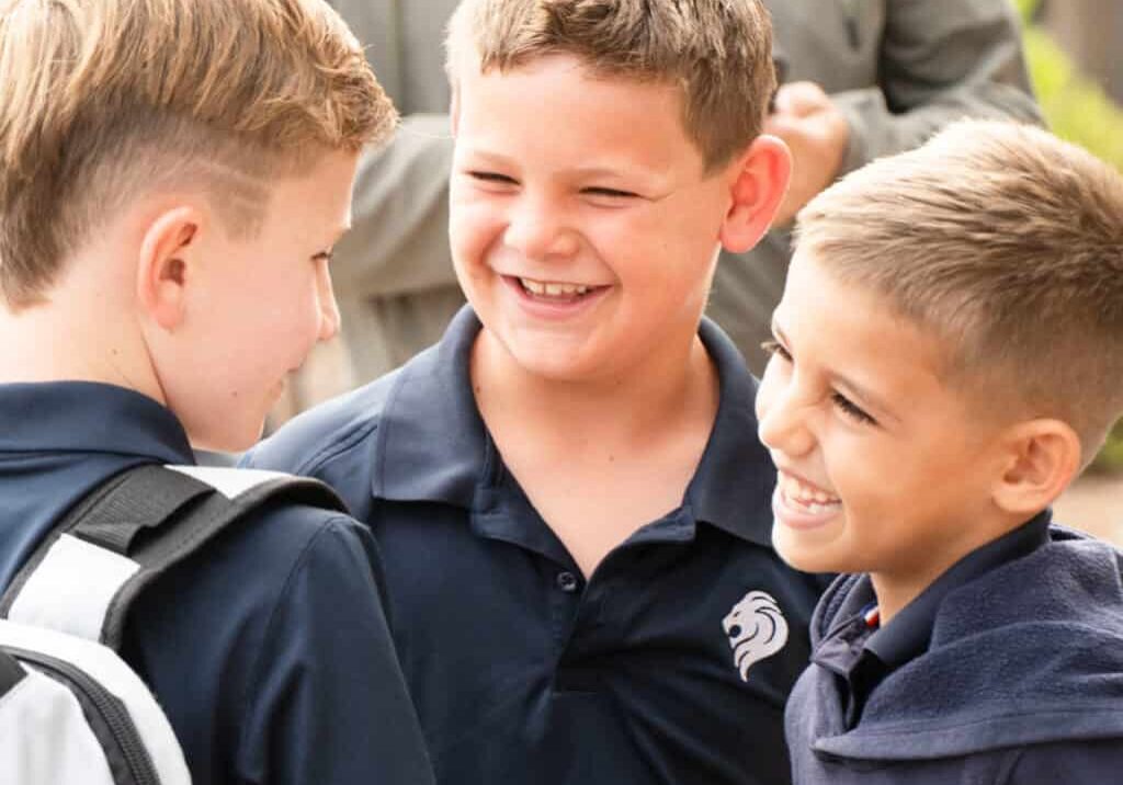 Three boys in SDJA blue polo shirts smile on the first day of school