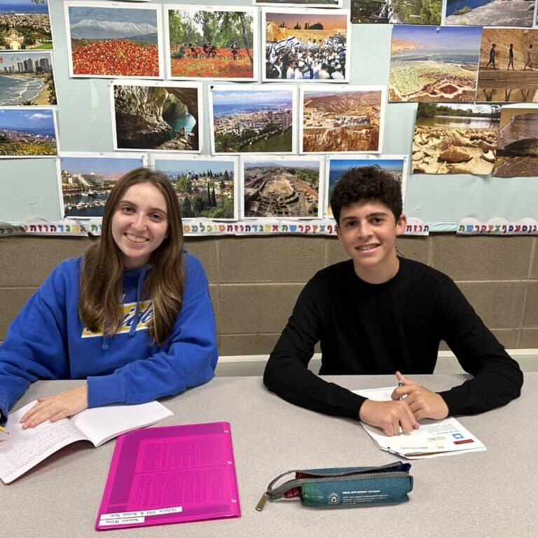 Two upper school students sit at a table with photos of Israel behind them