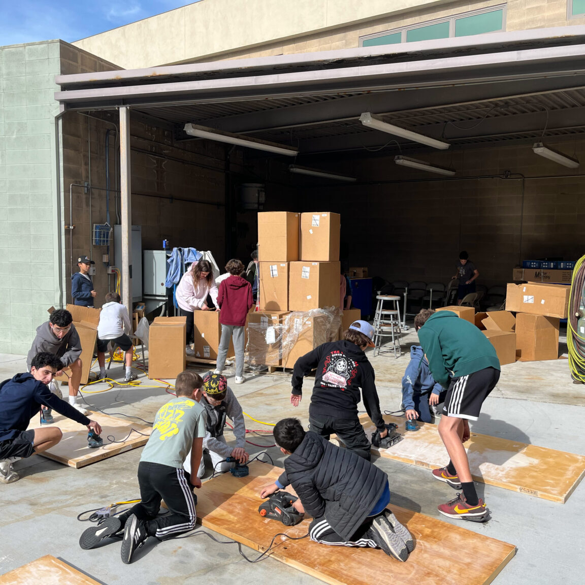 SDJA students using powertools to sand the surface of wooden blocks.
