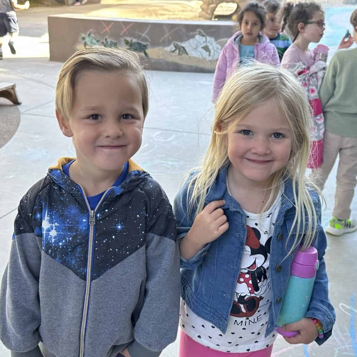 Two preschoolers stand together on the playground.