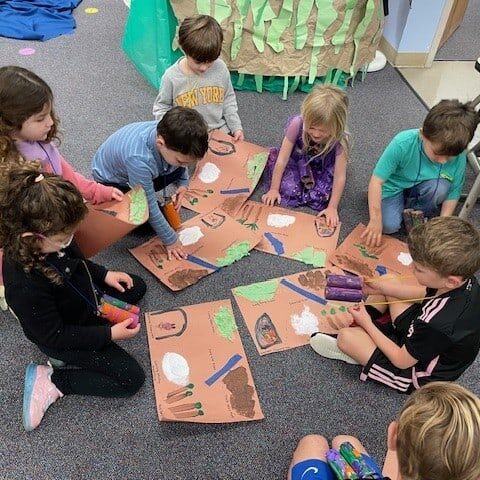 A group of preschoolers sit together on the ground while working on an art project.